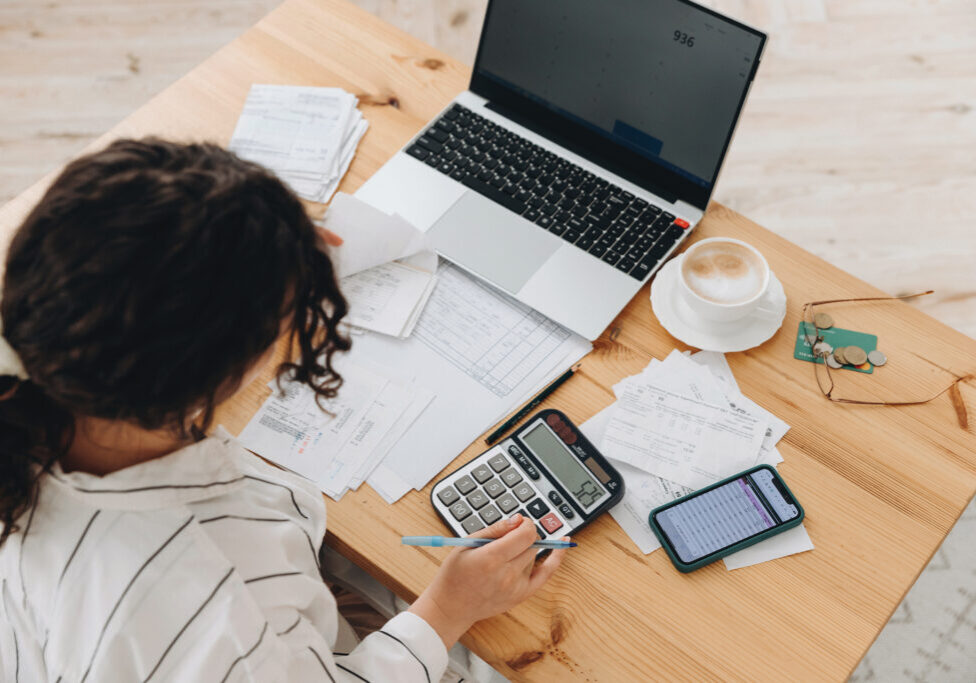 Top view of a woman working at home in the kitchen with financial papers, counting on a calculator, paying bills, planning a budget to save some money. Independent accounting, remote accountants.