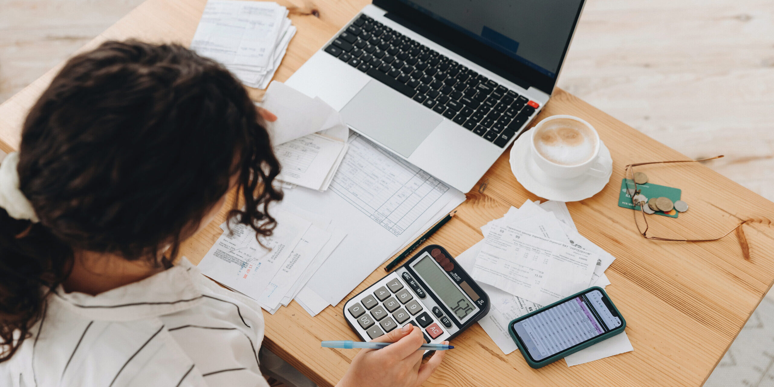 Top view of a woman working at home in the kitchen with financial papers, counting on a calculator, paying bills, planning a budget to save some money. Independent accounting, remote accountants.